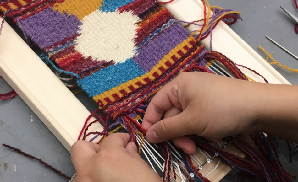 Hands weaving on a loom